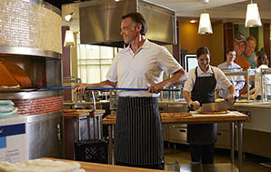 佩萨厨师穿着一支厨师®粉笔条纹围裙，将披萨放入木制烤箱
