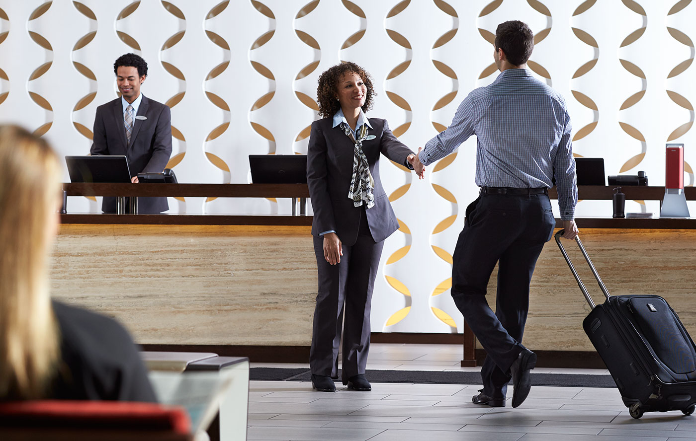 一个穿着合身长裤套装的女人正在和一个酒店的商务客户握手