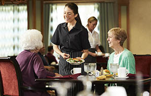 厨师衬衫的女服务器和粉笔条纹围裙，为两位女士提供汉堡